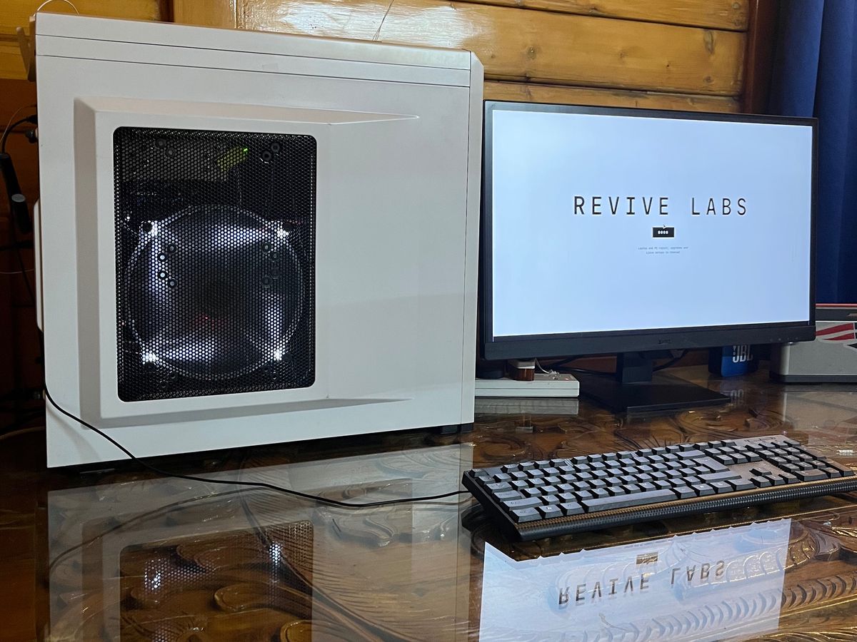 White PC tower with a side fan panel, next to a monitor showing the Revive Labs website
